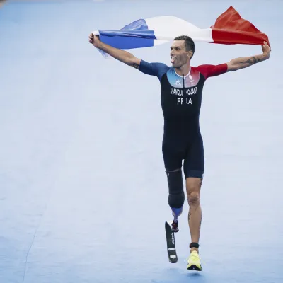 Alexis Hanquinquant, champion paralympique de para triathlon à Paris 2024 brandissant le drapeau français à l'arrivée de l'épreuve