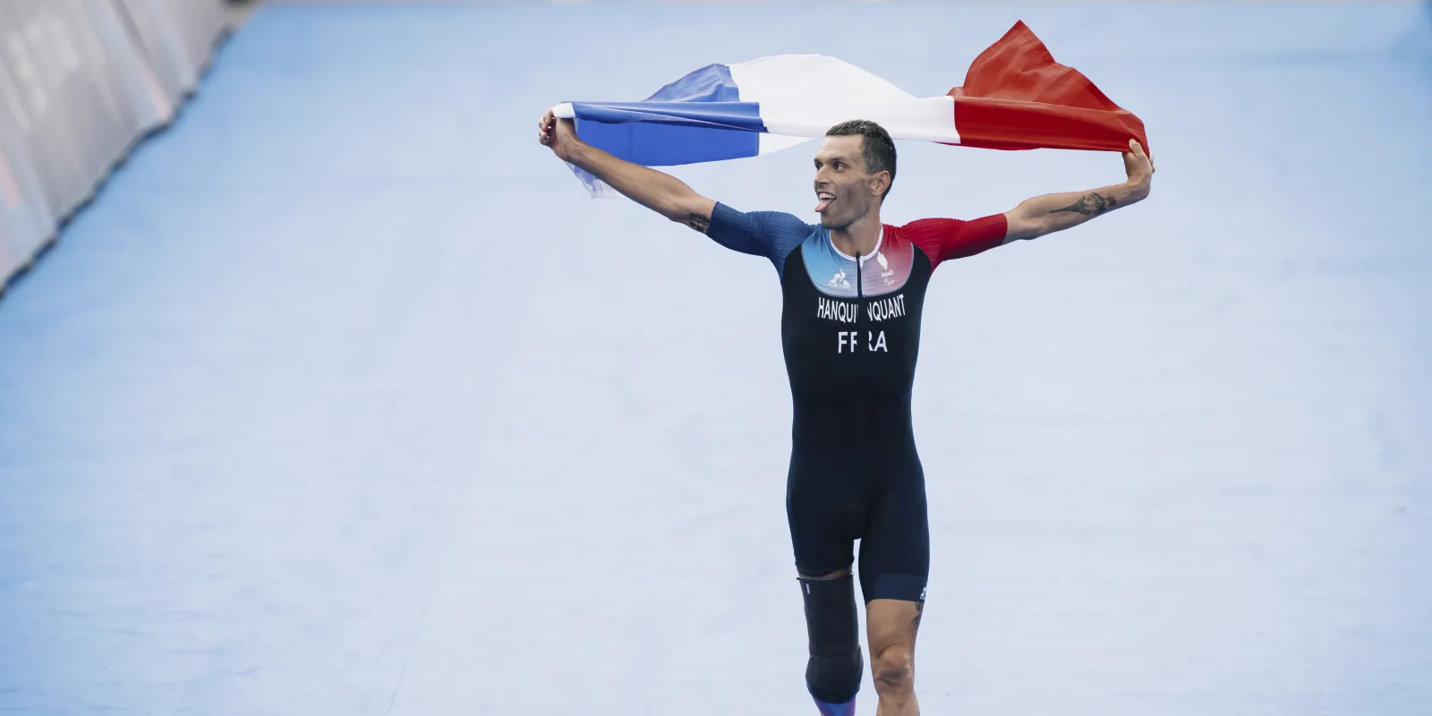 Alexis Hanquinquant, champion paralympique de para triathlon à Paris 2024 brandissant le drapeau français à l'arrivée de l'épreuve